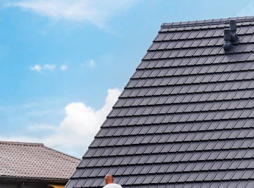 istockphoto-2207214237-612×612 (1) Construction site. Modern frame house. A construction worker is carefully placing roofing tiles on a sloped roof of a private building, vertical shot.